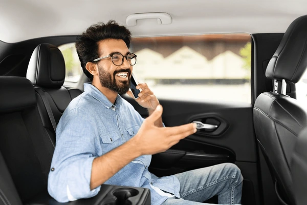 A smiling car owner sitting in the driver's seat of a modern vehicle, holding a phone and celebrating savings